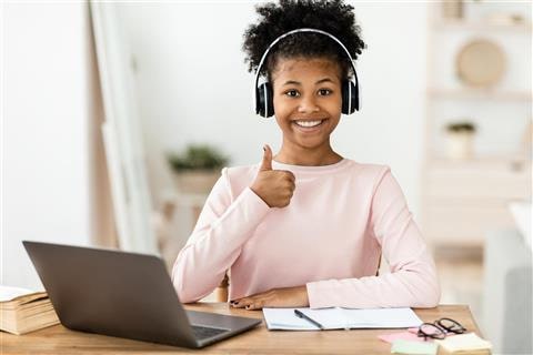 Educational Sites - Picture of student sitting next to a laptop with headphones on. She is looking at the camera, smiling, and giving a thumbs up.