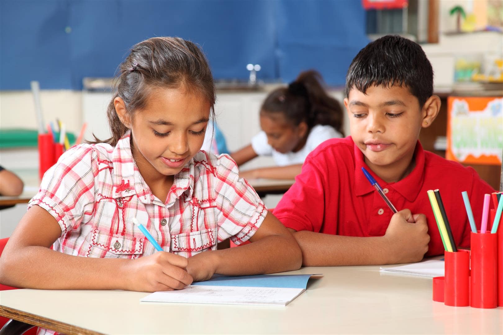 Student Resources - Image of two students working at a table. The girl is writing.